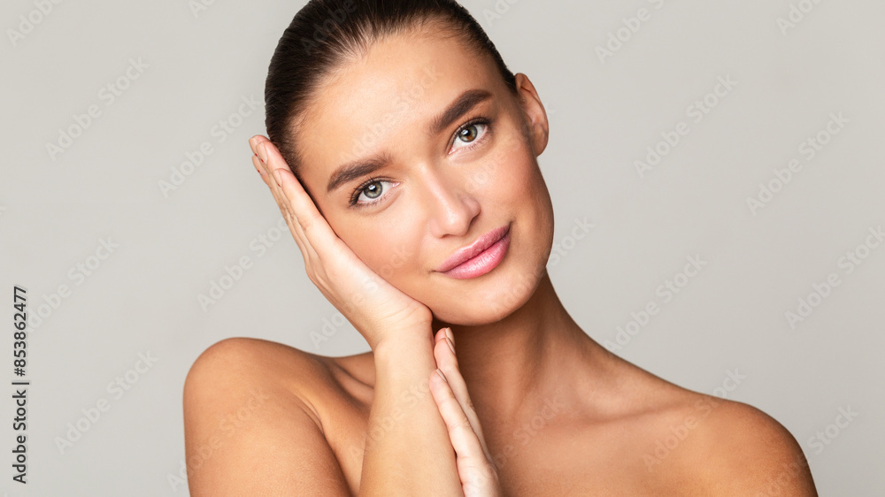 A beautiful young woman with long hair posing for a portrait. She is holding her hands against her cheeks, emphasizing her features. With a calm expression, she gazes directly at the camera. A beautiful young woman with long hair posing for a portrait. She is holding her hands against her cheeks, emphasizing her features. With a calm expression, she gazes directly at the camera.