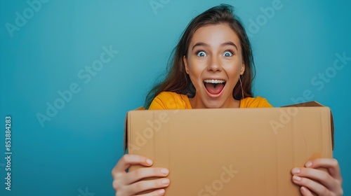 Astonished young woman with wide open eyes and mouth in excitement holding cardboard box