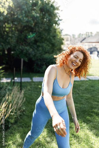 Obraz na plátně Portrait of cheerful redhead curly woman jogger beginner in blue leggings and cr