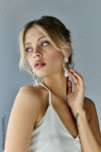 A young woman with blonde hair exudes elegance in a white dress while posing gracefully against a grey background.