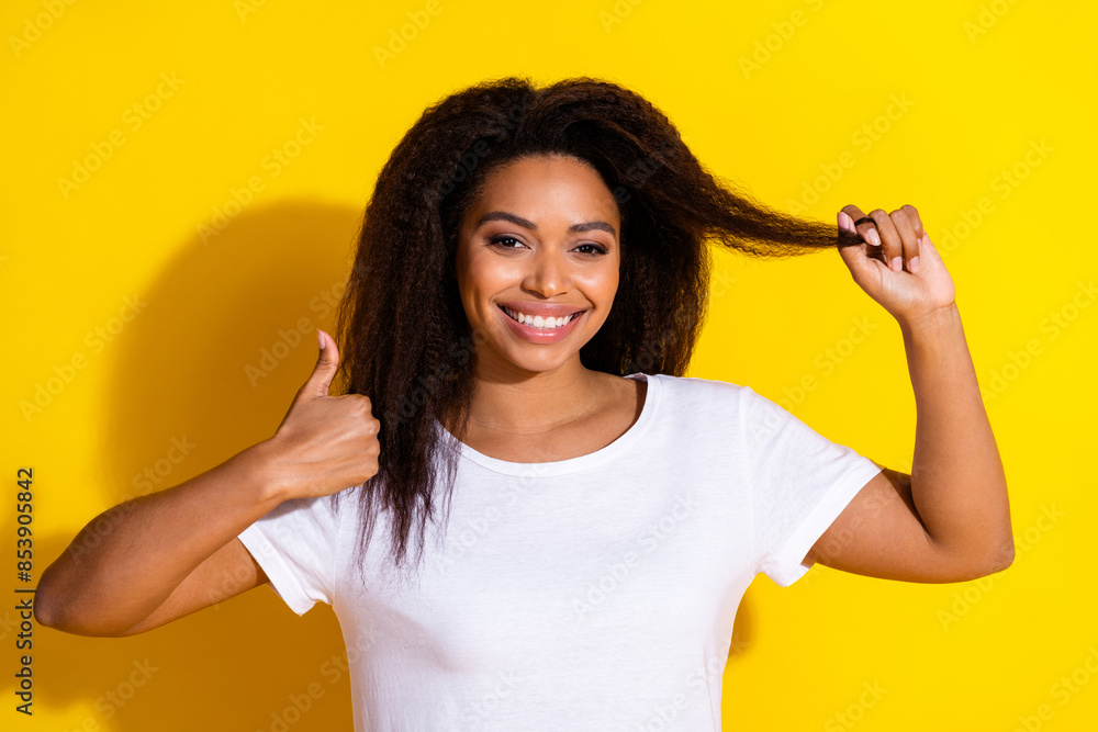 Portrait of nice young woman hold hair thumb up wear t-shirt isolated on yellow color background Portrait of nice young woman hold hair thumb up wear t-shirt isolated on yellow color background