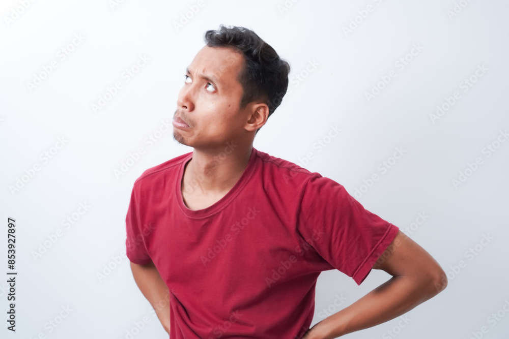 Fototapeta premium Young asian man posing in disbelief holding pigang with two hands, wearing red t-shirt isolated on white background. Shot in studio.