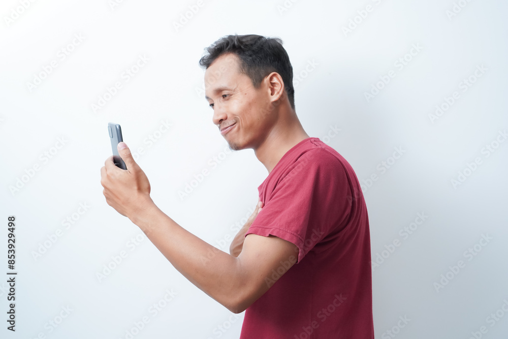 a young man wearing a red t-shirt holding a cellphone is calling happy expression on an isolated white background a young man wearing a red t-shirt holding a cellphone is calling happy expression on an isolated white background