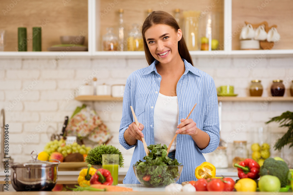 A woman smiles while mixing a salad in her kitchen, surrounded by fresh vegetables and a pot on the counter. A woman smiles while mixing a salad in her kitchen, surrounded by fresh vegetables and a pot on the counter.