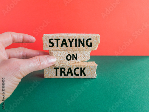 Concept words Staying on track on brick blocks on a beautiful green table red background. Businessman hand. Business, motivational and staying on track concept.