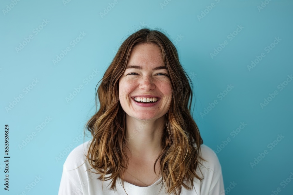 Fototapeta premium Portrait of a joyful caucasian woman in her 20s smiling at the camera while standing against pastel blue background
