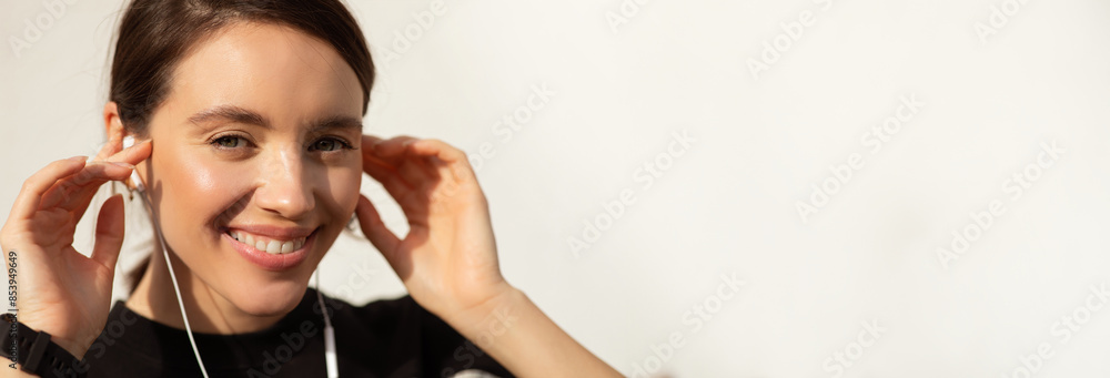 A young woman with long brown hair smiles while adjusting her white earbuds. Her skin is glowing, and she appears happy and relaxed, copy space A young woman with long brown hair smiles while adjusting her white earbuds. Her skin is glowing, and she appears happy and relaxed, copy space