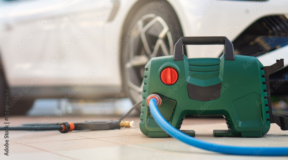 The photo shows a green and black pressure washer on the ground in front of a parked car The photo shows a green and black pressure washer on the ground in front of a parked car