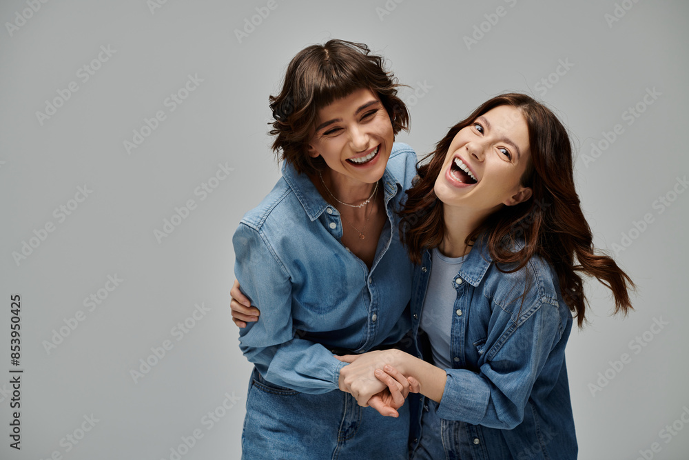 Two young women happily smile and hug each other, embodying love and fashion in their denim attire on a grey background. Lgbt couple Two young women happily smile and hug each other, embodying love and fashion in their denim attire on a grey background. Lgbt couple
