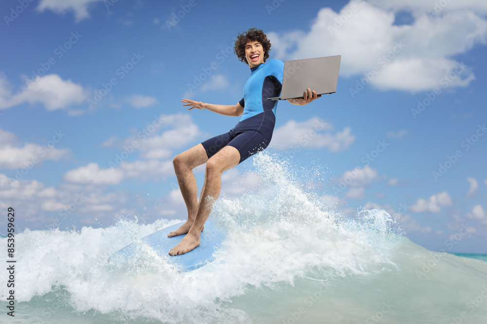 Young man in a wetsuit riding a surfboard with a laptop Young man in a wetsuit riding a surfboard with a laptop