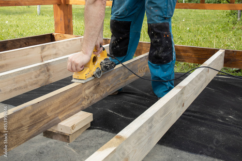 Wallpaper Mural A carpenter wearing blue pants sands a piece of wood using a power planer. The wood is part of a deck frame being built. Torontodigital.ca