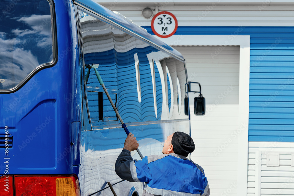 A man is cleaning a bus with a squeegee. The bus is parked in front of a building with a sign that says 33m A man is cleaning a bus with a squeegee. The bus is parked in front of a building with a sign that says 33m