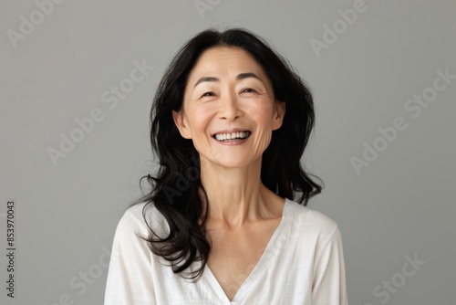 Portrait of a smiling asian woman in her 40s laughing on pastel gray background