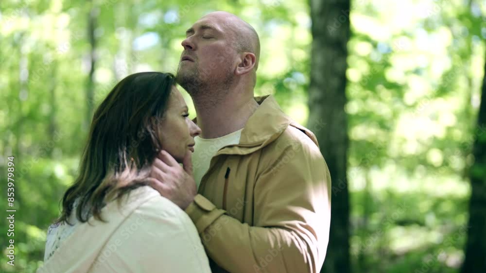 An adult couple enjoys a walk in the forest: a man with a bald head and a short beard, a woman with long dark hair. The forest is illuminated by soft daylight. An adult couple enjoys a walk in the forest: a man with a bald head and a short beard, a woman with long dark hair. The forest is illuminated by soft daylight.
