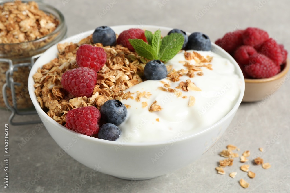 Tasty granola with berries and yogurt in bowl on grey textured table, closeup Tasty granola with berries and yogurt in bowl on grey textured table, closeup