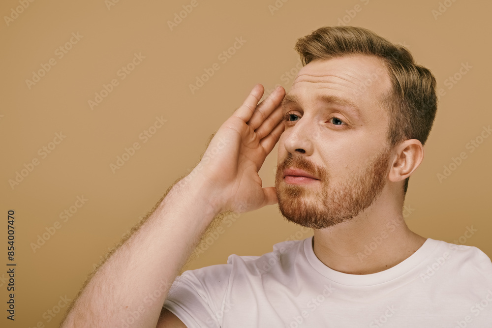 A stylishly dressed man with a beard places his hand on his face, contemplating deeply. A stylishly dressed man with a beard places his hand on his face, contemplating deeply.
