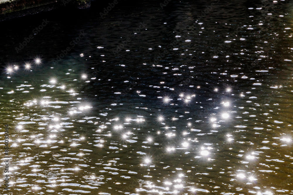 Sunlight reflects in many glittering stars from a dark water surface Sunlight reflects in many glittering stars from a dark water surface