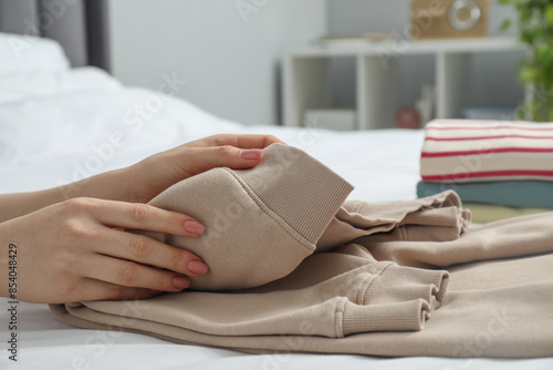 Woman folding clothes on bed indoors, closeup