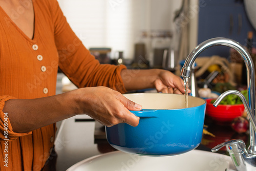 Close-up of a woman's hands holding a pot filling it with water in the kitchen sink