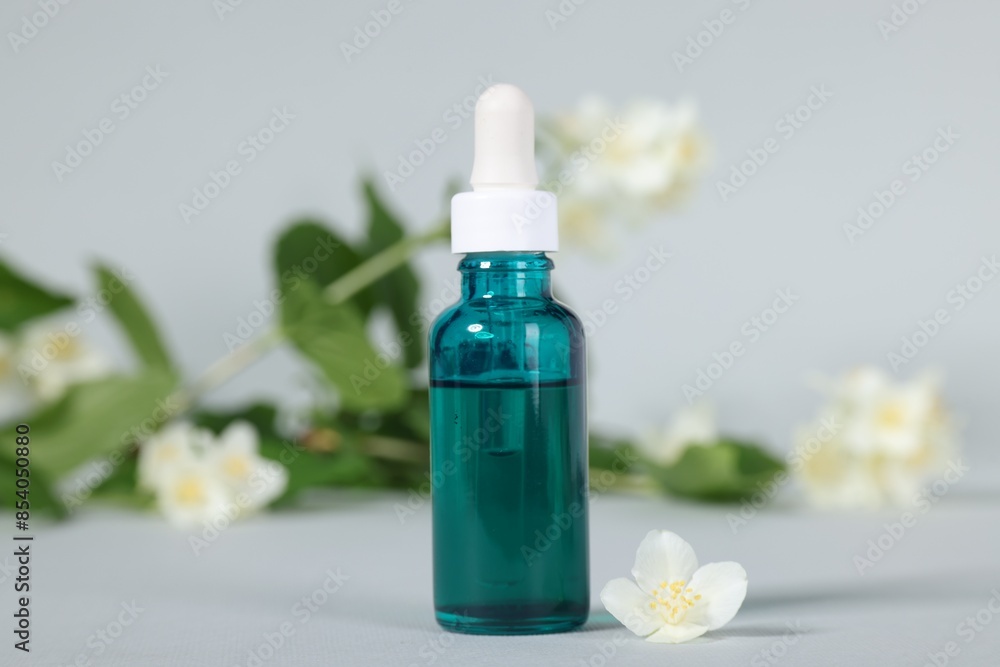 Essential oil in bottle and beautiful jasmine flowers on grey background, closeup Essential oil in bottle and beautiful jasmine flowers on grey background, closeup