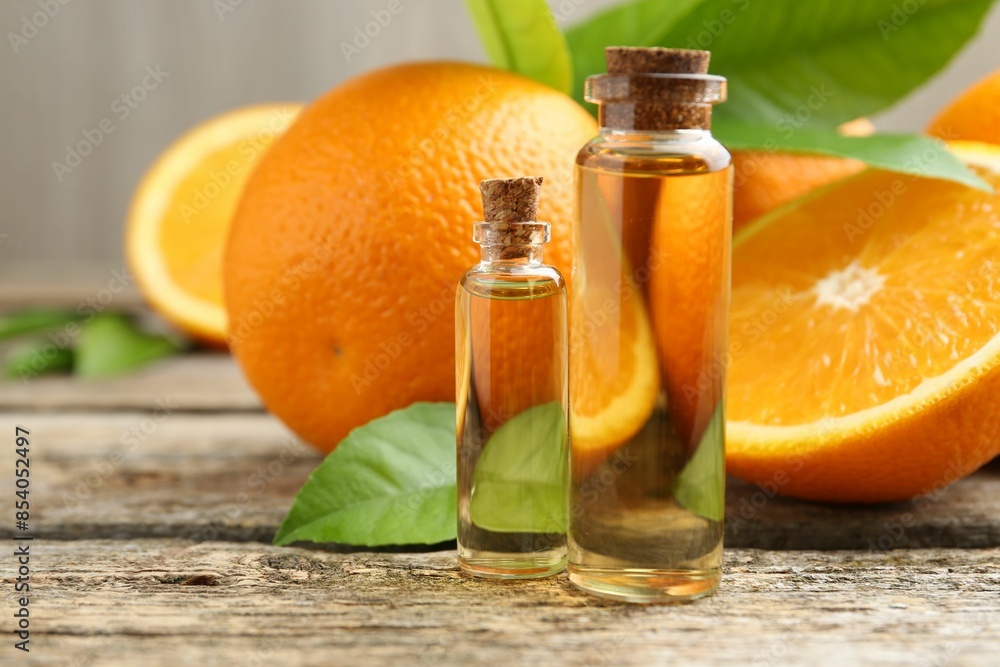 Essential oils in bottles, oranges and green leaves on wooden table, closeup Essential oils in bottles, oranges and green leaves on wooden table, closeup