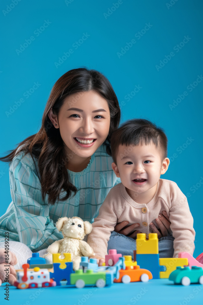 a Cheerful Asian Mother and Child: A mother and child playing together with building blocks, stuffed animals, and a puzzle on a blue studio background. They are dressed in casual, coordinated outfits a Cheerful Asian Mother and Child: A mother and child playing together with building blocks, stuffed animals, and a puzzle on a blue studio background. They are dressed in casual, coordinated outfits