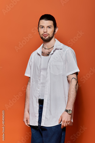 A handsome Caucasian man in trendy attire standing confidently in front of an orange wall.