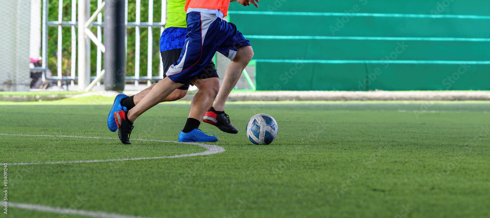 Obraz premium Soccer players in action during a game on a grass field, focusing on their legs and the ball.