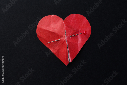 Halves of torn paper heart connected by sewing pin on black background, top view. Relationship problem concept
