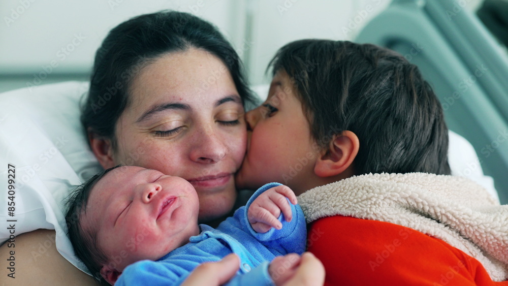 Loving family scene with a mother and her two children, including a newborn in a blue onesie and an older brother in a red jacket. Capturing the joy and affection of early family Loving family scene with a mother and her two children, including a newborn in a blue onesie and an older brother in a red jacket. Capturing the joy and affection of early family