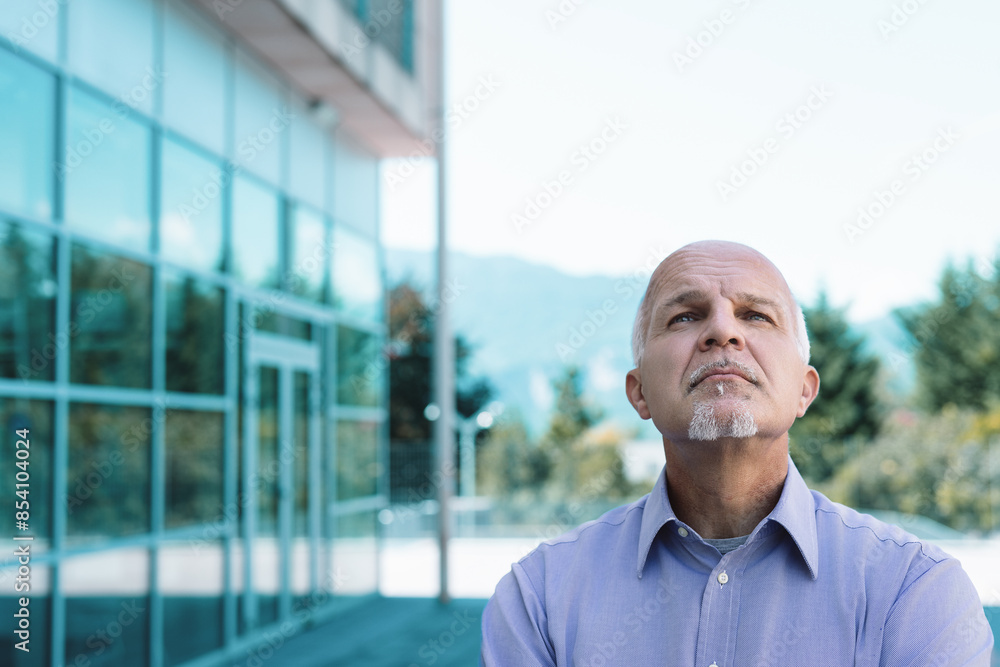 Senior businessman looking up and thinking in front of office bu Senior businessman looking up and thinking in front of office bu