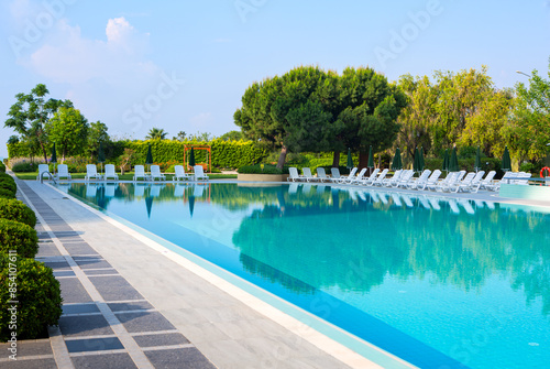 Resort hotel swimming pool with white lounge chairs and umbrellas; copy space