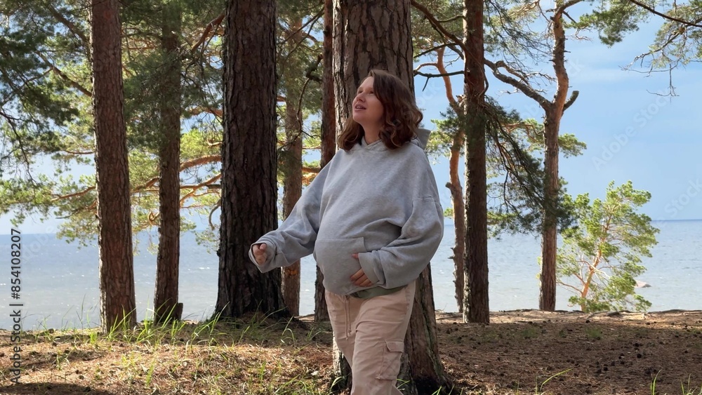 Young happy pregnant woman hiking walking outdoors in the summer forest on the beach near sea 