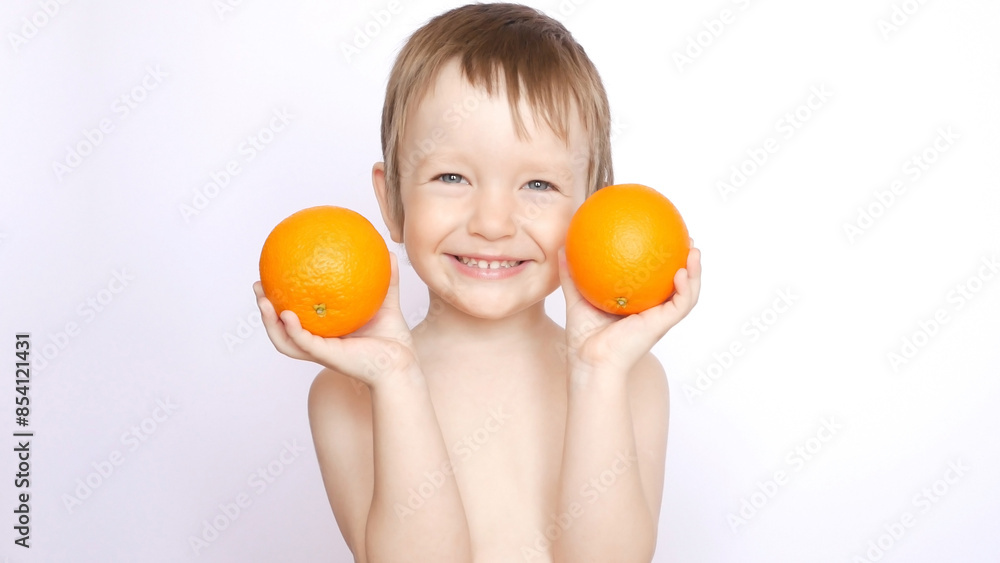 A happy cute boy poses with two fresh oranges in his hands A happy cute boy poses with two fresh oranges in his hands