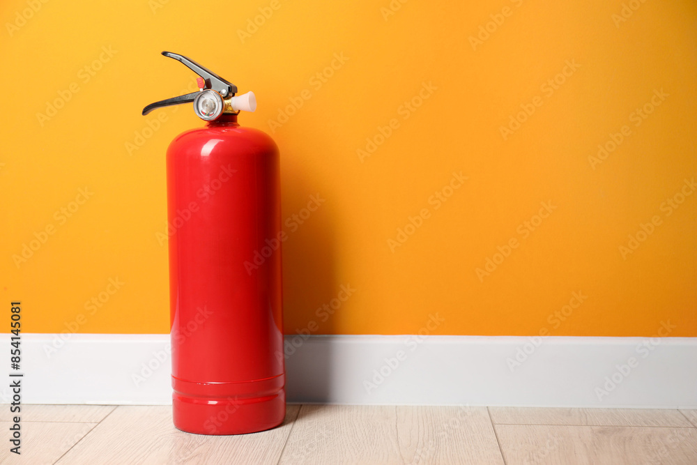 Obraz premium Fire extinguisher on floor near orange wall, space for text