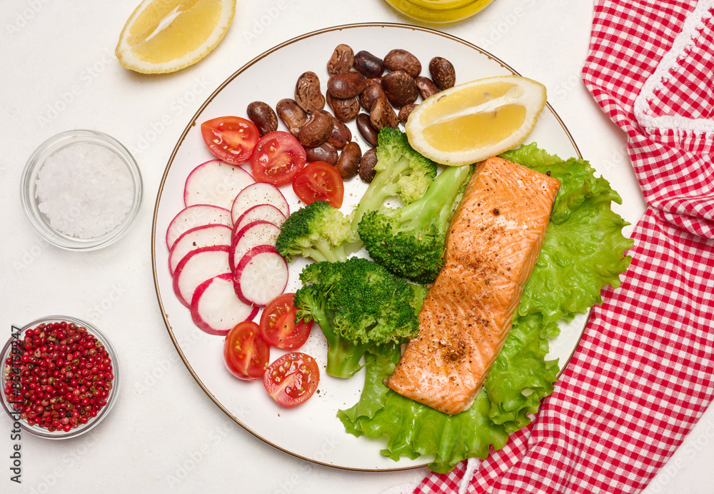 Healthy lunch with grilled salmon on green lettuce, next to vegetables, tomatoes, radishes, broccoli and a portion of beans. Healthy lunch with grilled salmon on green lettuce, next to vegetables, tomatoes, radishes, broccoli and a portion of beans.