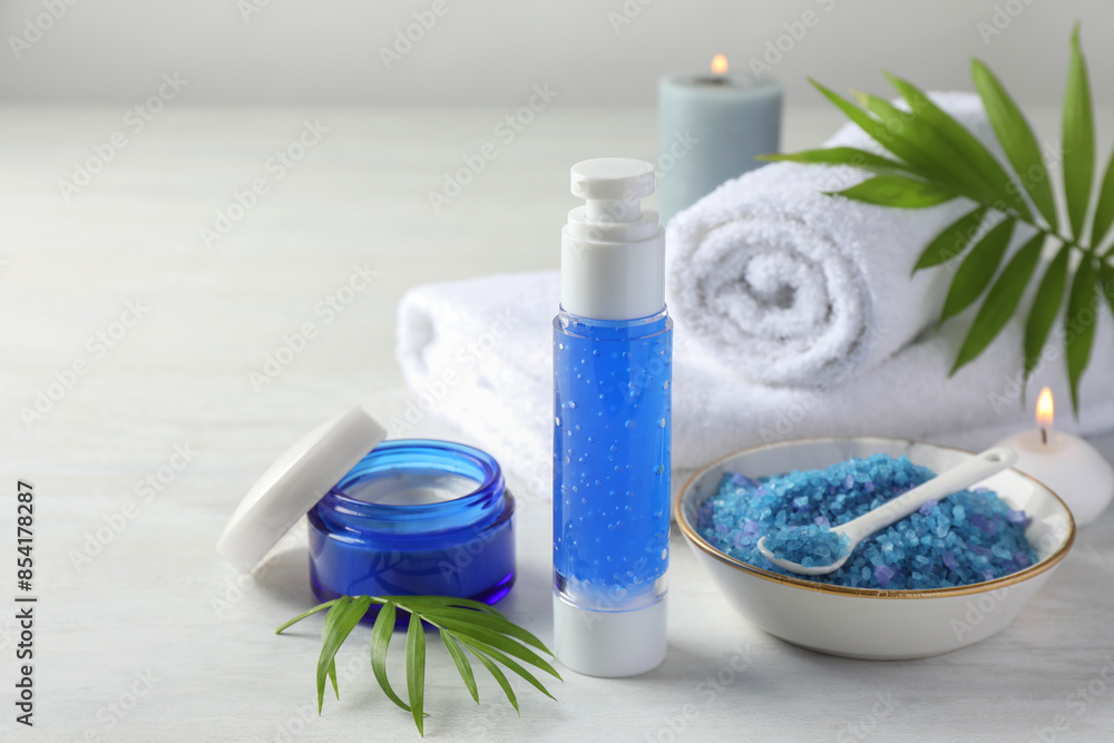Spa composition. Cosmetic products, towels, sea salt and burning candles on light table Spa composition. Cosmetic products, towels, sea salt and burning candles on light table