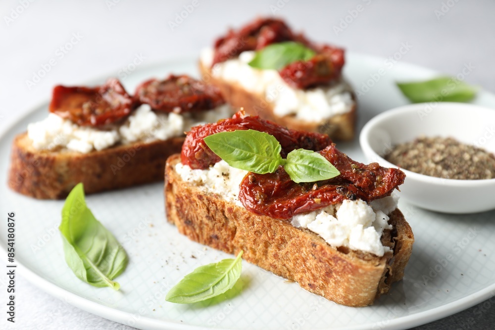 Delicious ricotta bruschettas with sun dried tomatoes, basil and milled pepper on light table, closeup