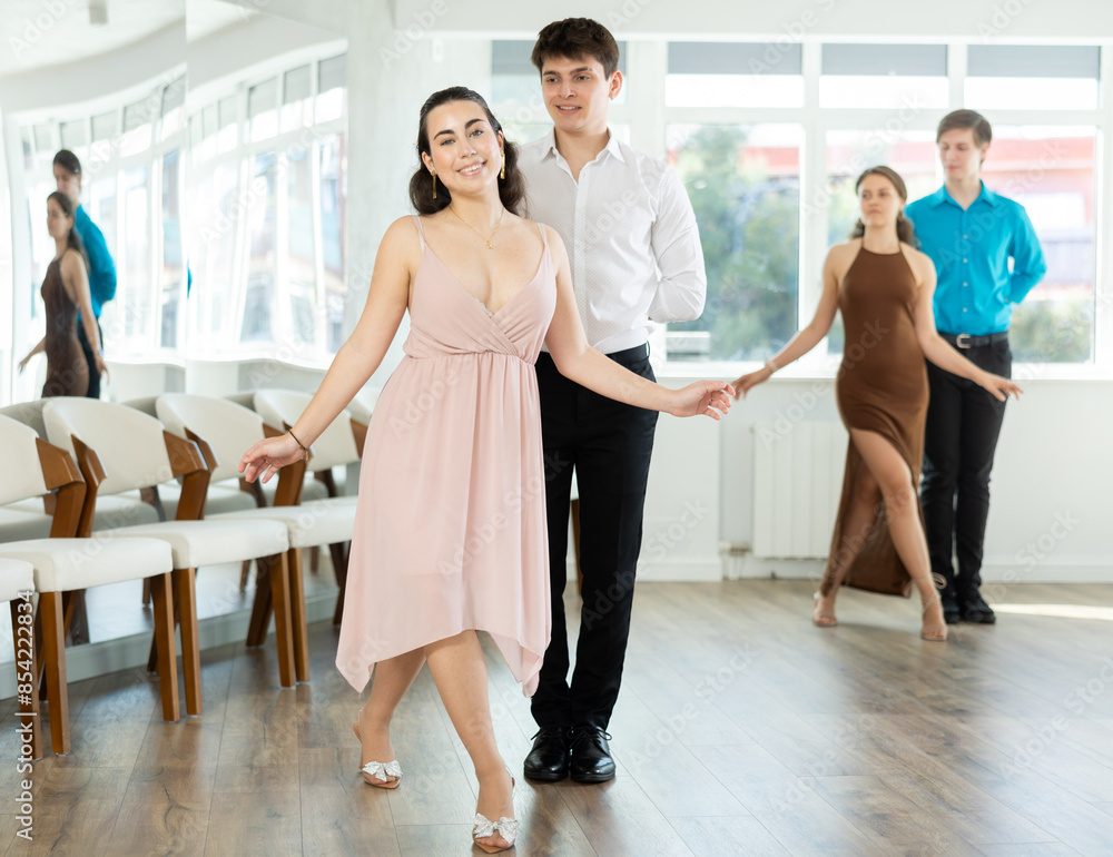 Fototapeta premium Enthusiastic young couple, elegant Latin American guy and dark-haired girl in formal wear, performing kizomba in studio, demonstrating dance characteristic sensual and connected movements..