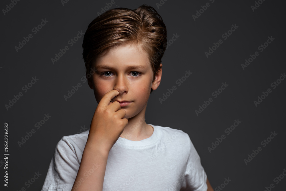 Child scratches his nose, portrait on dark background Child scratches his nose, portrait on dark background