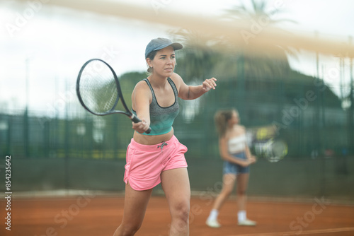 Two young athletic women playing doubles tennis on court © JackF