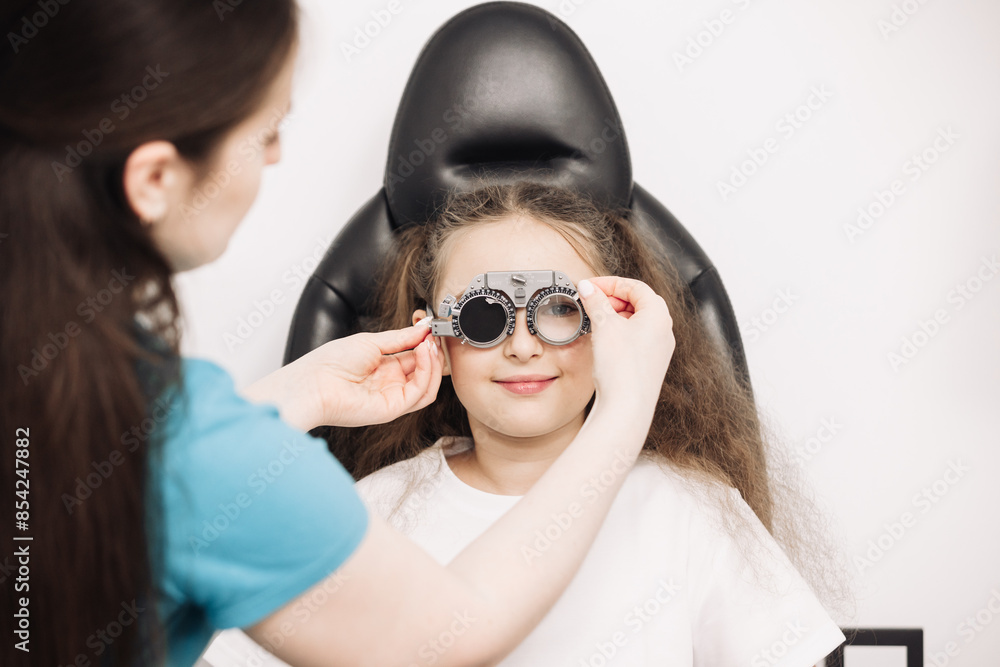 A female doctor holds special glasses to a patient for eye examination and lens selection in the clinic. Ophthalmology concept. An optician checks the vision of a small child. A female doctor holds special glasses to a patient for eye examination and lens selection in the clinic. Ophthalmology concept. An optician checks the vision of a small child.