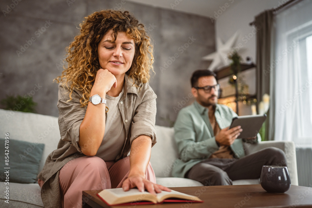 Girlfriend read a book while his boyfriend use tablet at home Girlfriend read a book while his boyfriend use tablet at home