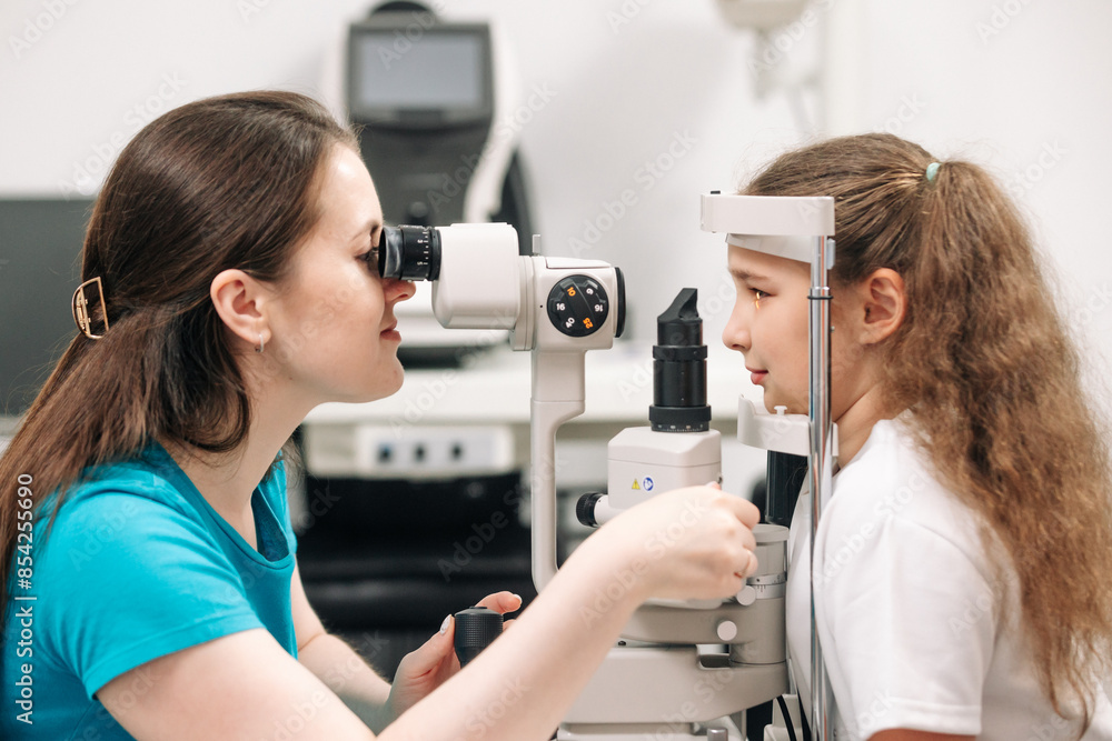 Close-up portrait of a happy little girl sitting in an optometrist's office while the doctor examines her eyesight in a modern clinic. Close-up portrait of a happy little girl sitting in an optometrist's office while the doctor examines her eyesight in a modern clinic.