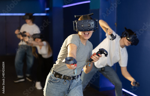 indoors, girl in virtual reality headset with joysticks in her hands actively moves and gesticulates while playing fighting game. Immersive Technologies XR VR AR MR photo