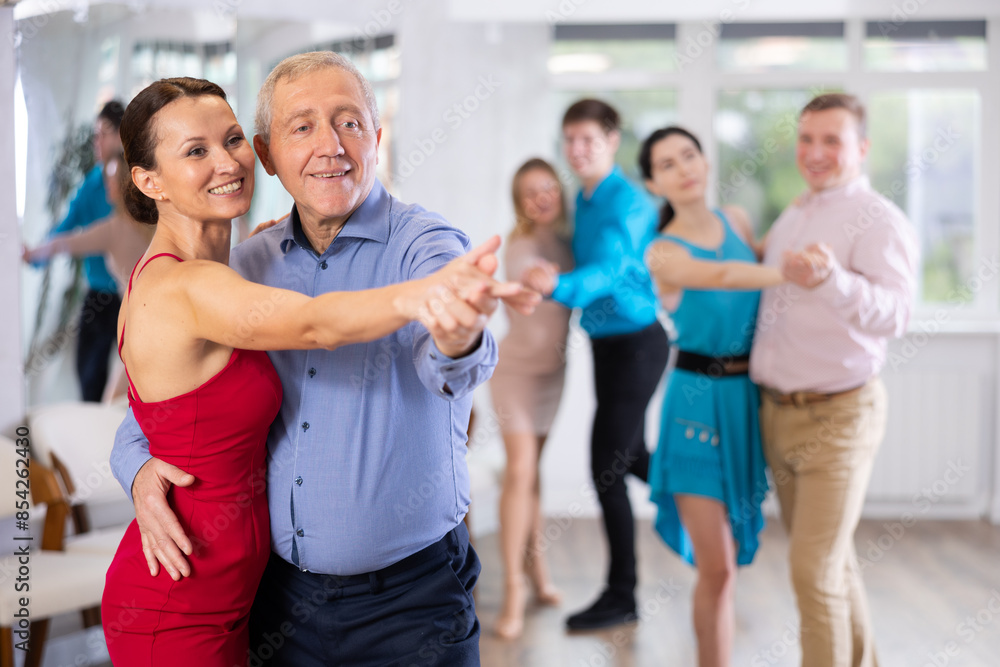 Obraz premium Smiling senior man and young woman dancing slow ballroom dance during group class in choreography studio..