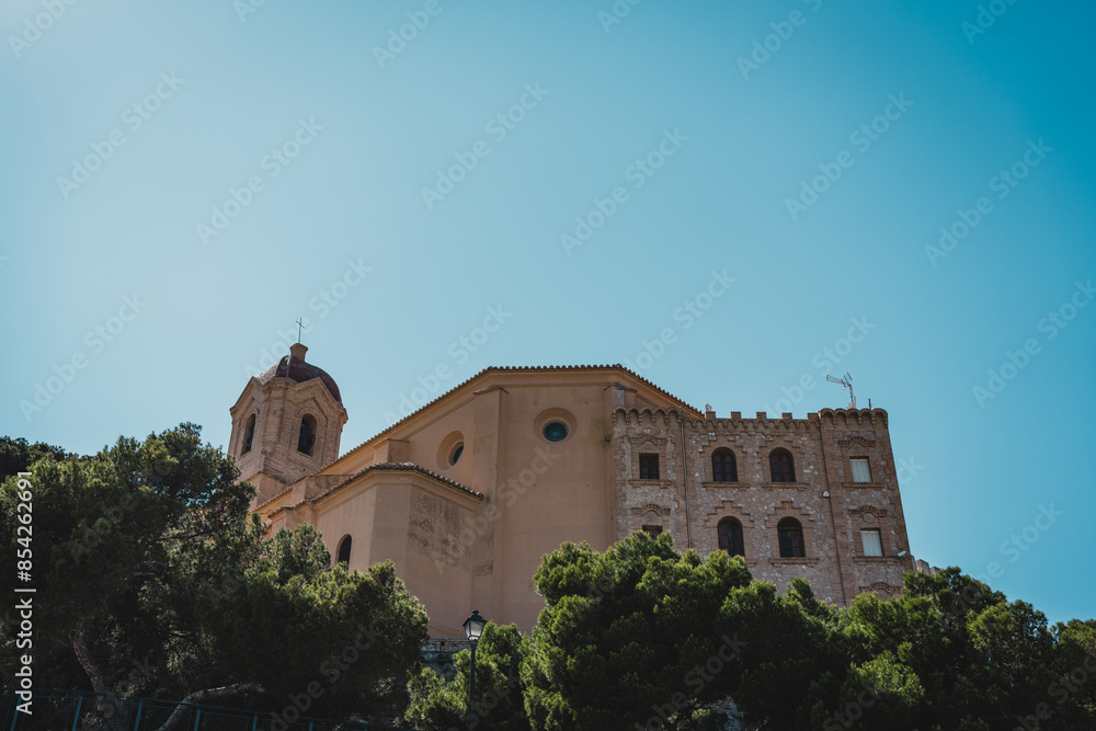 A historic church building with trees in the foreground and a clear blue sky above. Cullera Castle, Spain A historic church building with trees in the foreground and a clear blue sky above. Cullera Castle, Spain