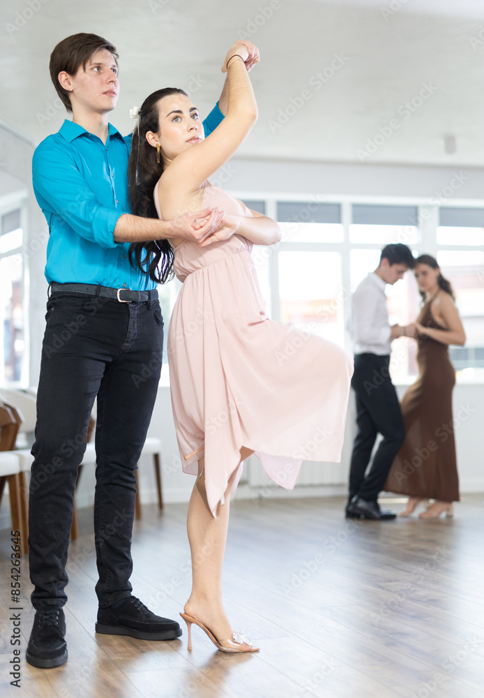 Fototapeta premium During rehearsal of reporting concert, guy and girl participants of dance workshop perform figure waltz. Several couples practice and hone their skills in performing waltz, classic slow dance style.