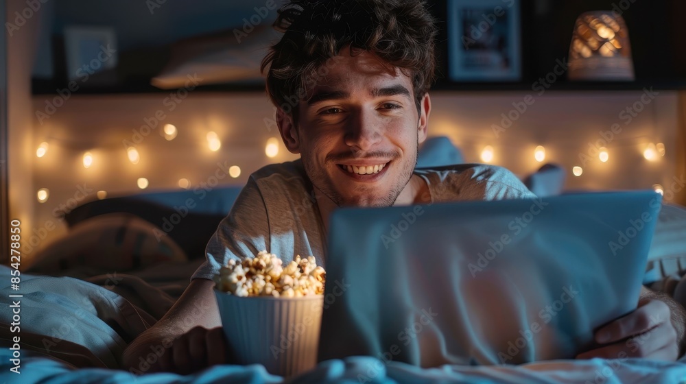 Cozy image of a smiling man enjoying a movie on his laptop in bed at night Cozy image of a smiling man enjoying a movie on his laptop in bed at night