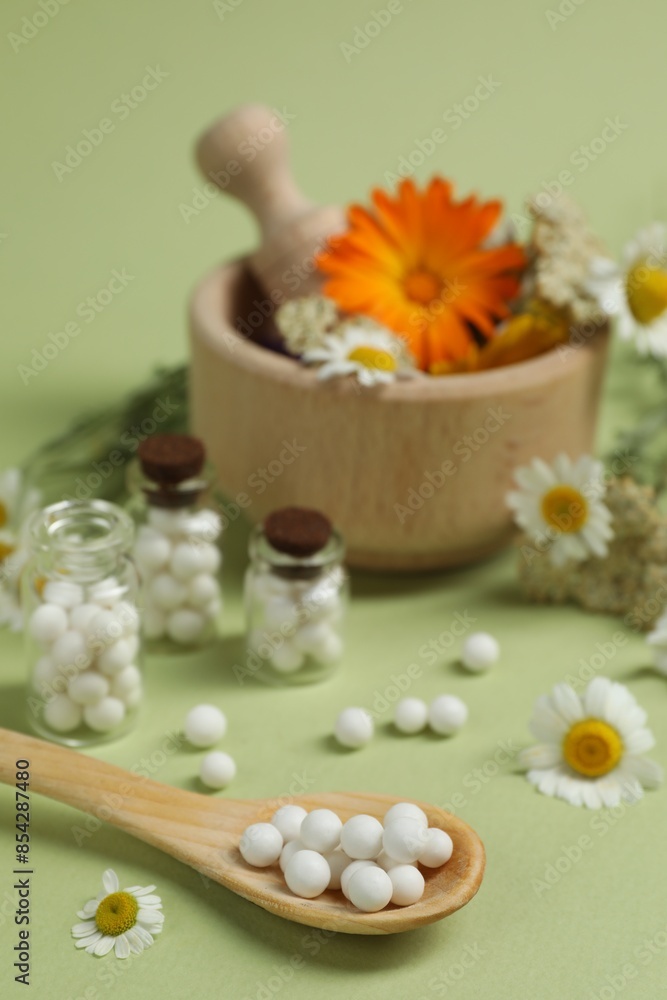 Homeopathic remedy, mortar and flowers on light green background, selective focus Homeopathic remedy, mortar and flowers on light green background, selective focus
